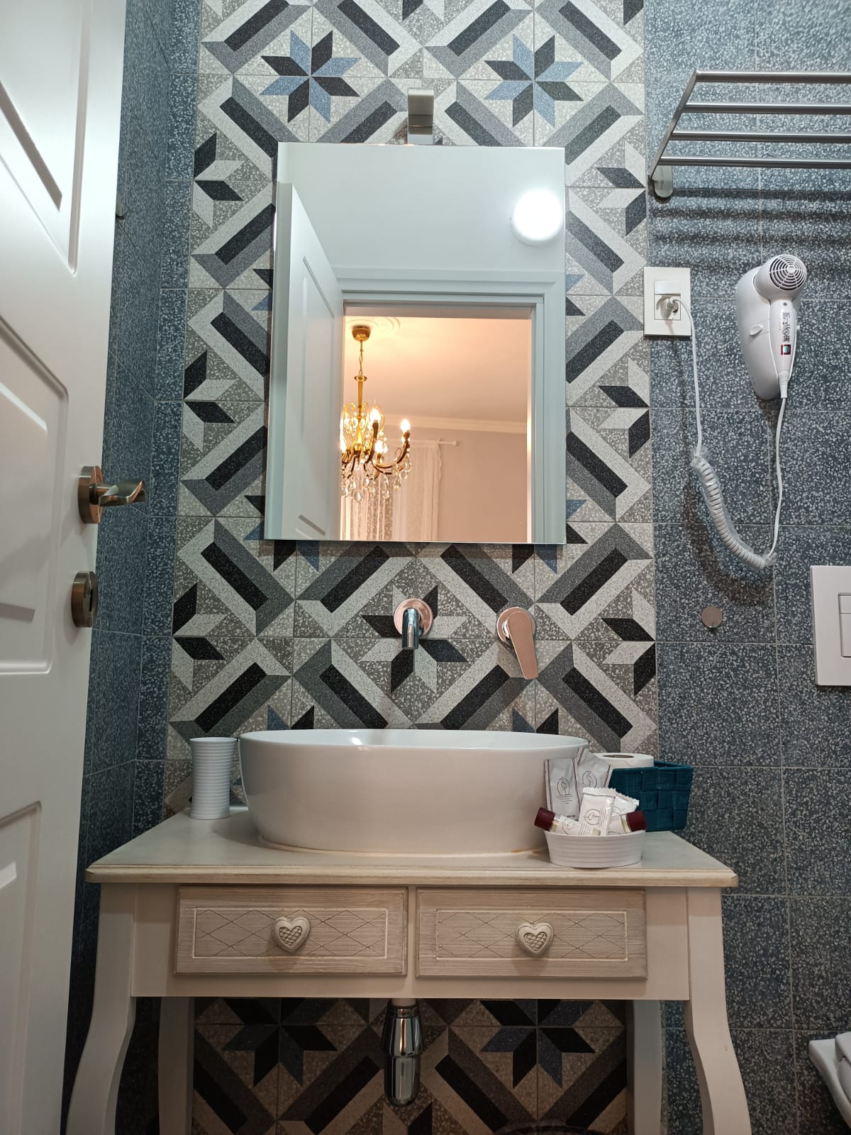 Bagno con piastrelle geometriche e lavabo bianco su mobile vintage